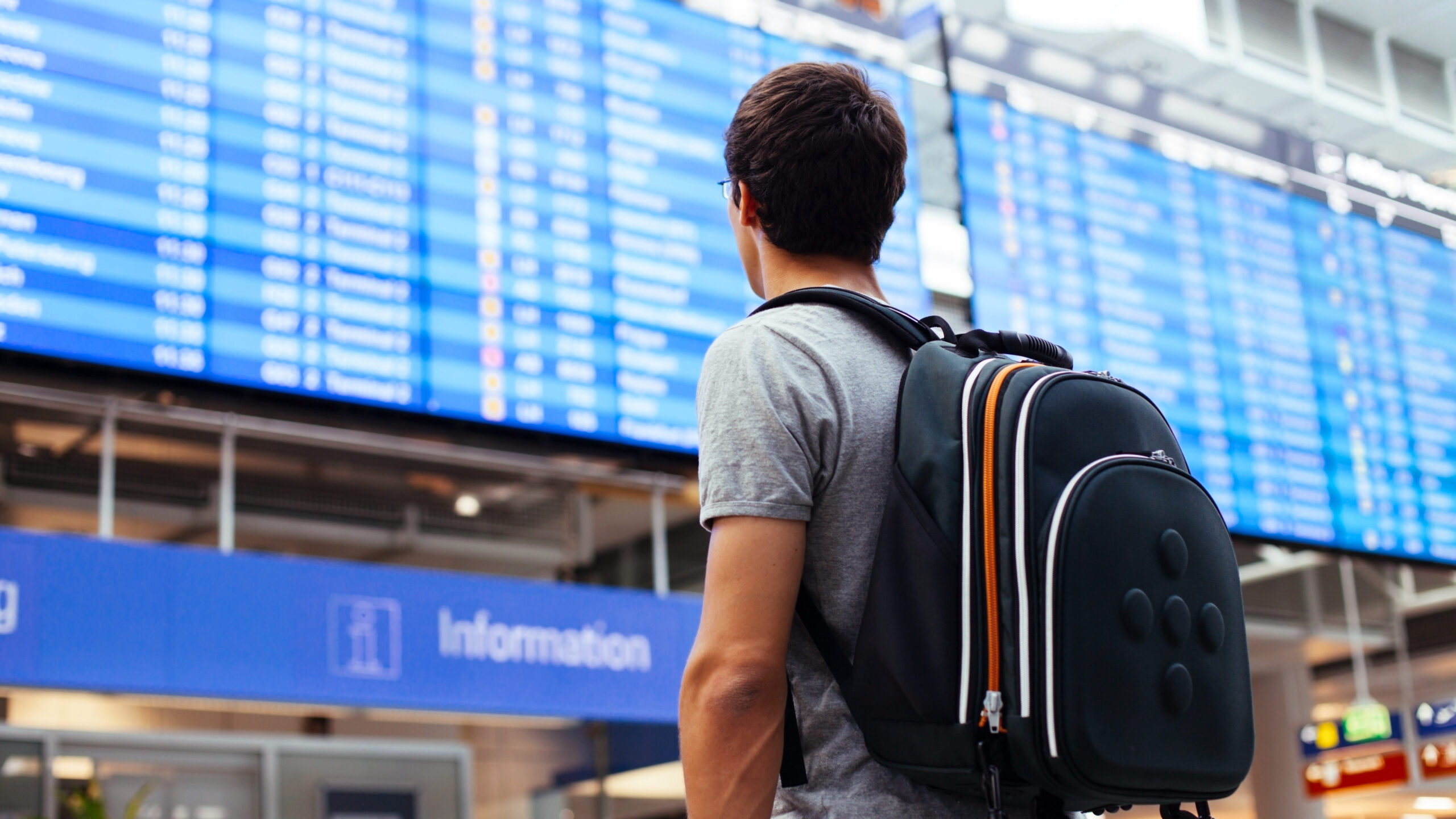 Young man with backpack in airport near flight timetable